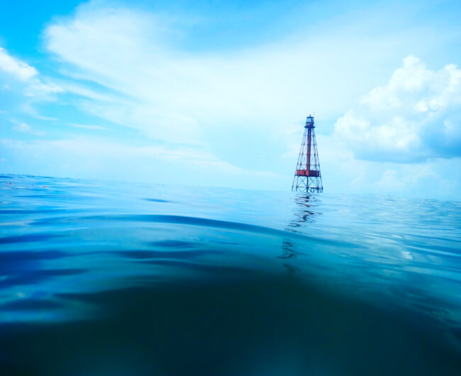 Deep blue water in the foreground, with a beacon rising above the water in the distance.