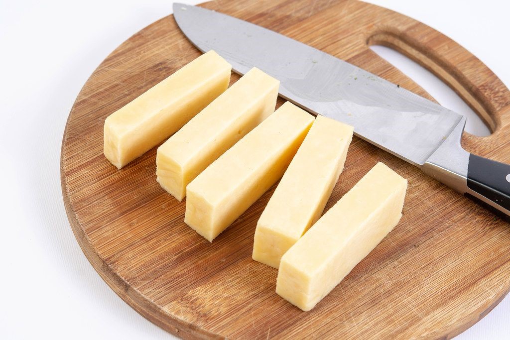 Photo of cheese with a knife on a wooden cheeseboard.