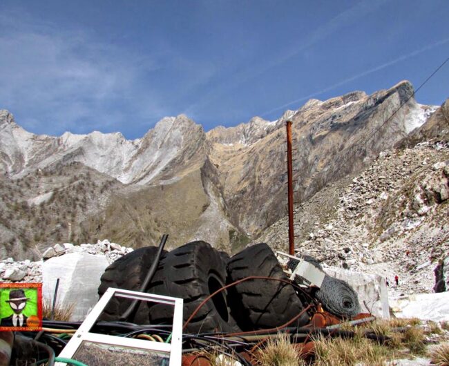 Piles of trash, including old tires, in the foreground; the Alps in the background.