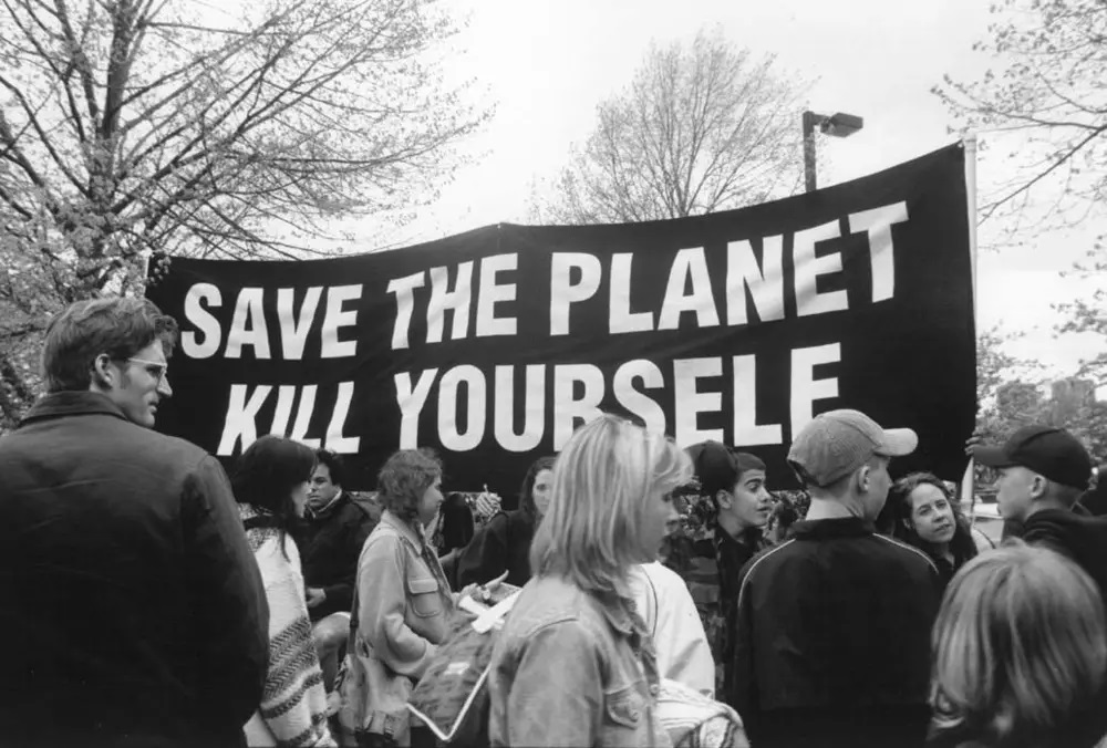 A black and white image of a crowd with a banner reading "Save the Planet, Kill Yourself."